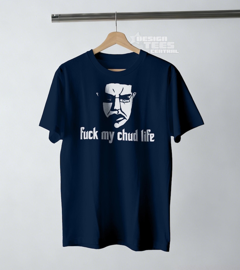 May include: Navy blue t-shirt with a white graphic of a face wearing glasses and the text "fuck my chud life". The shirt is hanging on a wooden hanger.