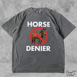Peut inclure: T-shirt gris avec l'inscription blanche "HORSE DENIER", un cheval marron dans un cercle rouge barr&eacute;. Le t-shirt a des manches courtes et un col rond.