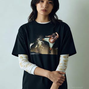 May include: Black t-shirt featuring a graphic of a person kicking in a body of water. The person is wearing camouflage shorts. The shirt is layered over a white long-sleeve shirt with a yellow and white pattern. The text "DESIGN TEES CENTRAL" is at the bottom.