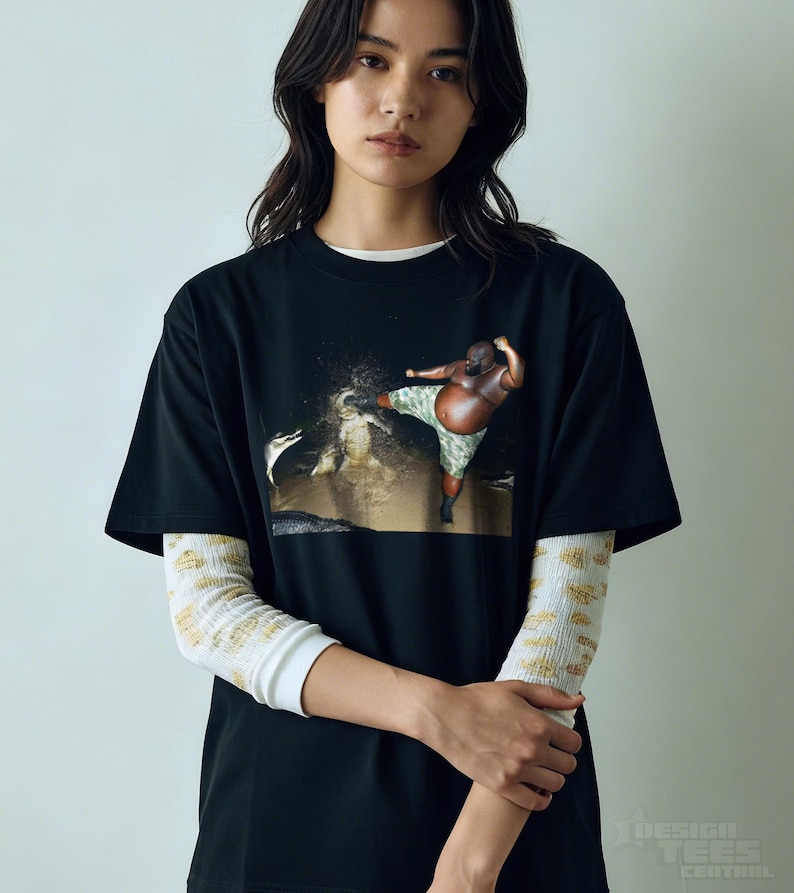 May include: Black t-shirt featuring a graphic of a person kicking in a body of water. The person is wearing camouflage shorts. The shirt is layered over a white long-sleeve shirt with a yellow and white pattern. The text "DESIGN TEES CENTRAL" is at the bottom.