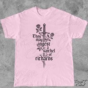 以下が含まれることがあります： 薄いピンク色のTシャツ。黒いグラフィックで、剣、バラ、そして「Thou may ingest a satchel of richards」というテキストが描かれています。デザインはTシャツの中央に配置されています。