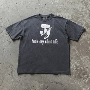 May include: Dark gray t-shirt with a white graphic of a face and the text "fuck my chud life". The shirt has short sleeves and a crew neck. The graphic is centered on the front of the shirt.