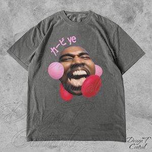 May include: A grey t-shirt featuring a graphic of Kanye West's face surrounded by pink and red balloons. The text "カービィ ye" is printed on the shirt.