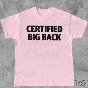 May include: A pale pink t-shirt featuring the text "CERTIFIED BIG BACK" in bold black lettering. The shirt has a round neck and short sleeves. The graphic is centrally placed on the chest.