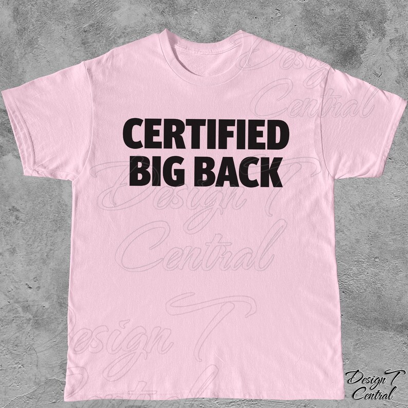 May include: A pale pink t-shirt featuring the text "CERTIFIED BIG BACK" in bold black lettering. The shirt has a round neck and short sleeves. The graphic is centrally placed on the chest.