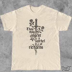 以下が含まれることがあります： クリーム色のTシャツ。黒い剣、バラ、テキストのグラフィックが描かれています。テキストはゴシック体で「Thou may ingest a satchel of richards」と書かれています。Tシャツはクルーネックで半袖です。