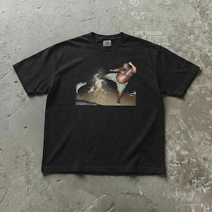 May include: Black t-shirt featuring a humorous image of a person kicking in water. The person is wearing camouflage shorts. The shirt has the text "DESIGN TEES CENTRAL" printed on the top right corner.