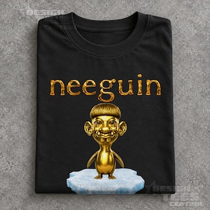 May include: A black t-shirt featuring the gold-coloured text "neeguin" above a graphic of a metallic gold character with a bowl-cut hairstyle, large ears, and prominent front teeth, standing on a light blue textured ice-like base.