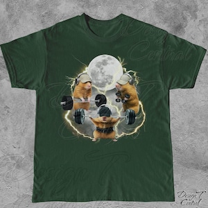 May include: Dark green t-shirt featuring a humorous graphic of hamsters lifting weights. The design includes three hamsters with hats and headphones, lifting barbells under a full moon, with lightning bolts around them. The text "Design Central" is at the bottom.