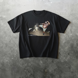 May include: Black t-shirt featuring a graphic of a person kicking in water. The person is wearing camouflage shorts. The shirt has a crew neck and short sleeves. The image is centered on the shirt.
