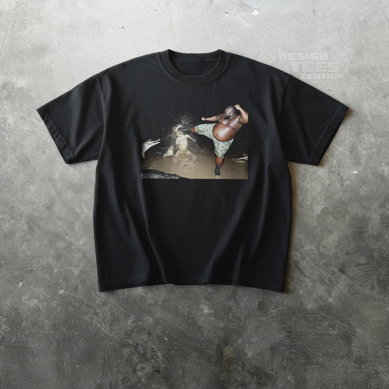 May include: Black t-shirt featuring a graphic of a person kicking in water. The person is wearing camouflage shorts. The shirt has a crew neck and short sleeves. The image is centered on the shirt.