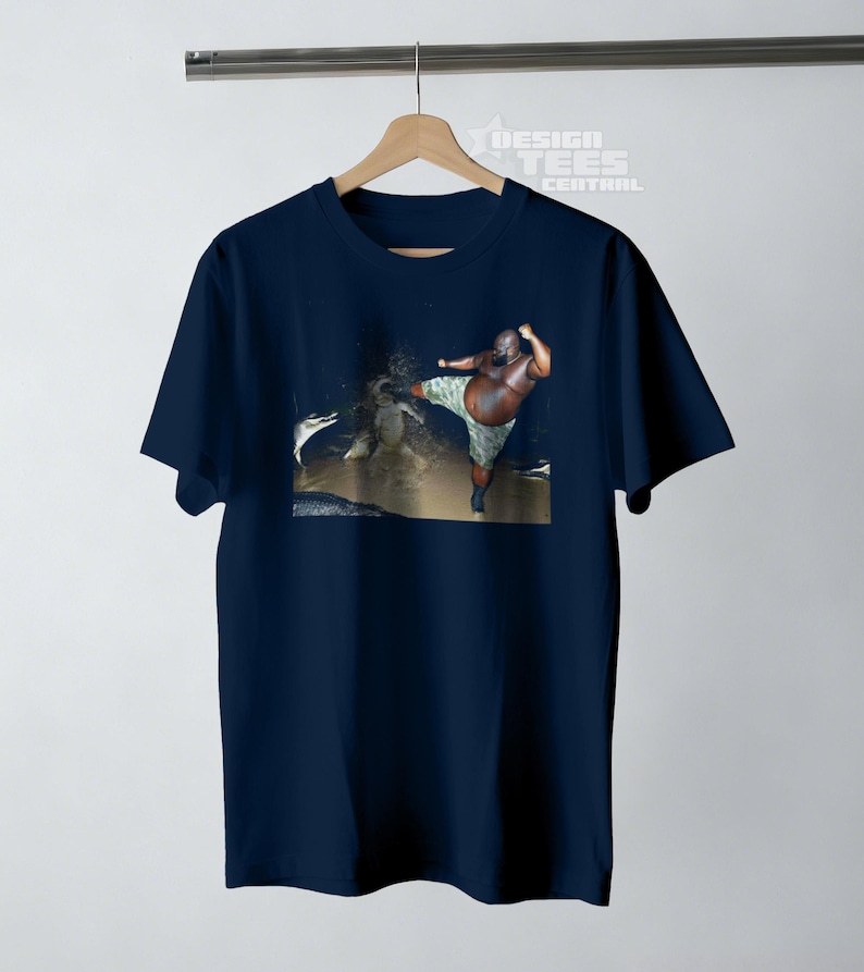 May include: Navy blue t-shirt featuring a graphic of a person kicking. The person is wearing camouflage shorts. The shirt is hanging on a wooden hanger. The text "DESIGN TEES CENTRAL" is visible.