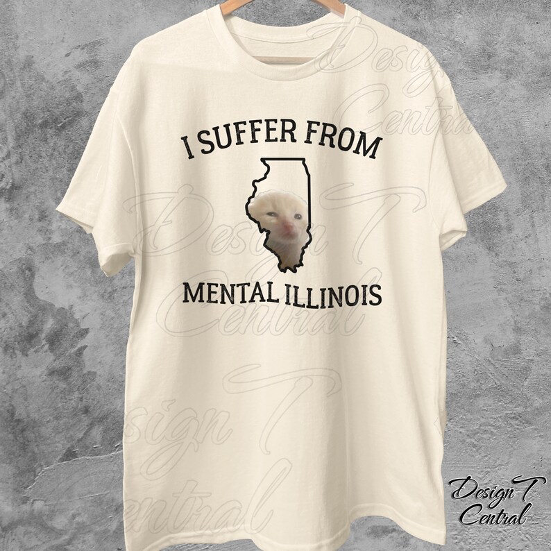 May include: A beige t-shirt with black text that reads "I suffer from mental Illinois". The text is overlaid on a black outline of the state of Illinois. A white cat's face is visible inside the outline of the state.