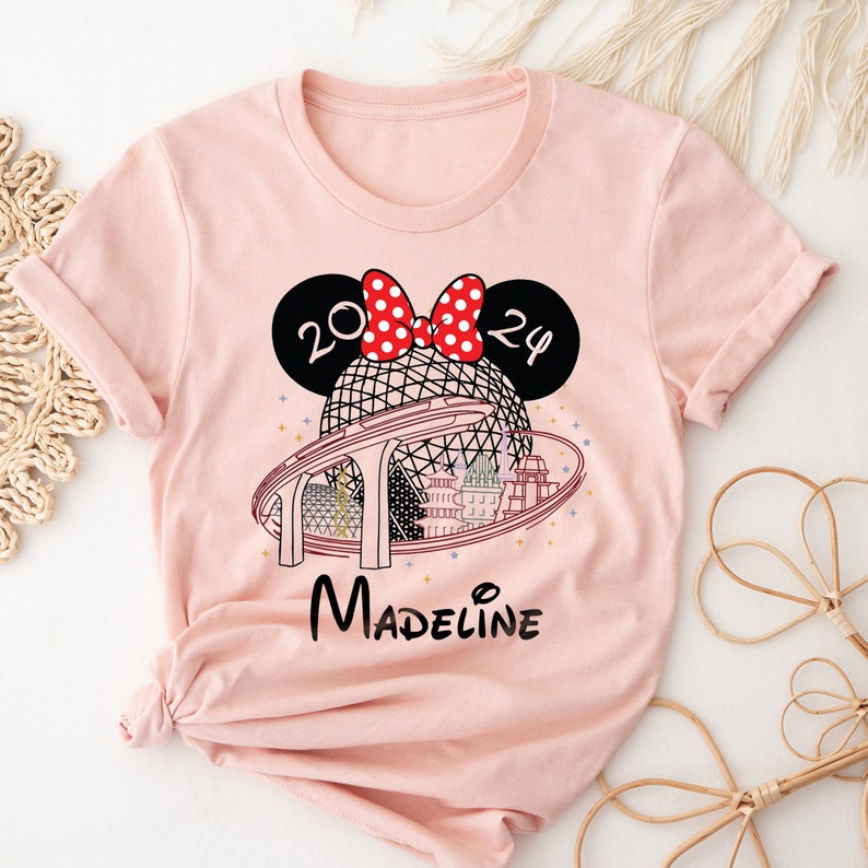 Pu&ograve; includere: Maglietta rosa con un designo di orecchie di Topolino in bianco e nero con un fiocco rosso e pois bianchi. Le orecchie hanno i numeri 20 e 24. Il design include anche un contorno in bianco e nero della corsa Spaceship Earth a Epcot con il testo "Madeline" sotto.
