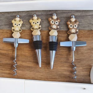 May include: Set of three wine bottle stoppers with a deer design. Each stopper features a different colored deer with a wooden base and a silver metal top. The set also includes two silver metal wine openers.