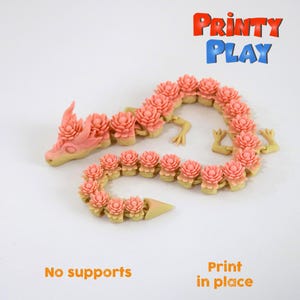 May include: A 3D printed pink and beige dragon with a flower design. The dragon is articulated and can be posed in different ways. The text "Print in place" and "No supports" is visible in the image.