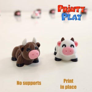 以下が含まれることがあります： ピンクの鼻と黒い蹄を持つ、茶色と白の2つの3Dプリントされたおもちゃの牛。茶色の牛は白い角を持っています。白い牛には黒い斑点があります。「Printy Play」の文字が右上隅にあります。「No supports」と「Print in place」の文字が下にあります。