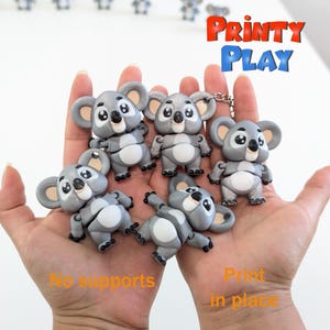May include: Five gray koala figurines with articulated limbs, printed in place. The koalas have white bellies and black eyes. The text "PRINTY PLAY" is visible in the background.