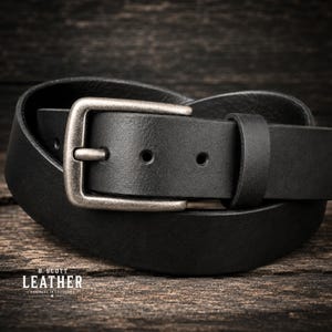 May include: A black leather belt featuring a rectangular, weathered silver-tone metal buckle and a single matching leather keeper loop. The text B. SCOTT LEATHER HANDMADE IN CALIFORNIA is printed in white in the lower left corner of the image.