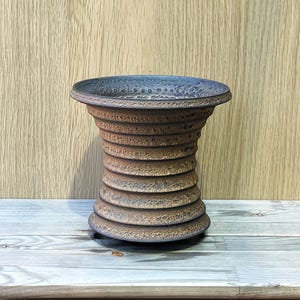 May include: A handcrafted, textured ceramic vase with a unique, ribbed design. The vase features a dark blue rim and a gradient of brown and tan hues. The vase is a decorative piece for home decor.