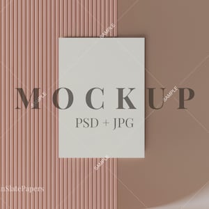 May include: A mockup design featuring a white rectangular card with the word "MOCKUP" and "PSD + JPG" printed on it. The card is set against a textured, vertical-striped pink background and a solid brown backdrop.
