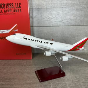 May include: A white and red model airplane with the text "KALITTA AIR" on the side. The model is a B747-400, mounted on a stand. A red box with the text "TAMPICO 1933, LLC MODEL AIRPLANES" is in the background.