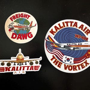 May include: Three stickers featuring Kalitta Air branding. One sticker has a cartoon airplane with the text "FREIGHT DAWG". Another sticker shows a 747-400 plane with the text "KALITTA AIR THE VORTEX". The third sticker shows a plane with the text "KALITTA AIR".