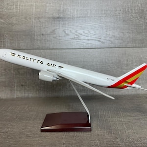 May include: A white model airplane with red and gold accents. The airplane is labeled "Kalitta Air" and "N778CK". The model is displayed on a dark wood stand.