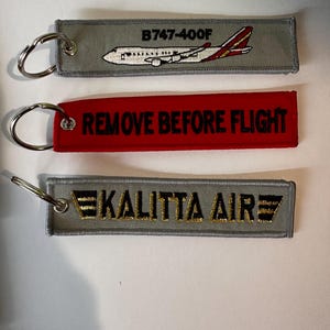 May include: Three embroidered keychains. One gray keychain features a B747-400F airplane design. A red keychain reads "REMOVE BEFORE FLIGHT." Another gray keychain displays "KALITTA AIR" in gold and black.