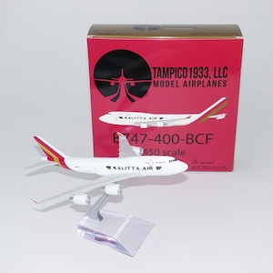 May include: A white and red Kalitta Air B747-400-BCF model airplane with a stand, in front of a red box. The box has the text "Tampico 1933, LLC Model Airplanes" and an image of a plane.