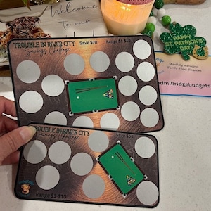 May include: Two green and brown cards with a pool table design and a grid of circles. The text on the cards reads "Trouble in River City Savings Challenge" and "Save $70" and "Save $53". The cards are printed with a wood grain background.