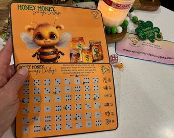 Puede incluir: Un tablero de juego Honey Money Savings Challenge con una ilustración de abeja de dibujos animados. El tablero presenta una cuadrícula de cuadrados con iconos de dados y un icono de tarro de miel. El texto "Honey Money Savings Challenge" está impreso en el tablero.