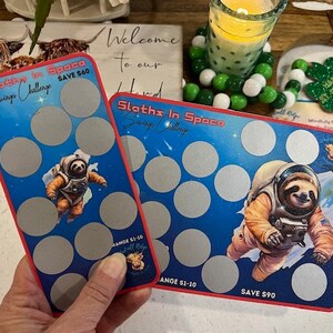 Puede incluir: Dos tarjetas azules y rojas con un perezoso en un traje espacial en cada tarjeta. Las tarjetas tienen una cuadrícula de círculos. El texto en las tarjetas dice "Sloths In Space Savings Challenge" y "SAVE $60" y "SAVE $90".