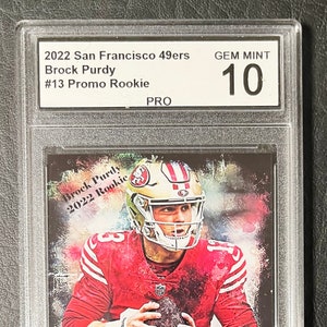 May include: A graded trading card featuring a colorful illustration of Brock Purdy, a football player for the San Francisco 49ers. The card is labeled "2022 San Francisco 49ers Brock Purdy #13 Promo Rookie" and "GEM MINT 10".