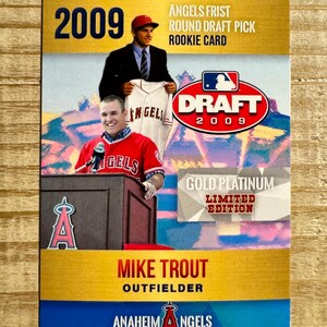 May include: A baseball rookie card featuring Mike Trout, an outfielder for the Anaheim Angels. The card has a gold and blue design with the text "2009" and "Draft 2009". The card also includes the text "Angels Frist Round Draft Pick Rookie Card".