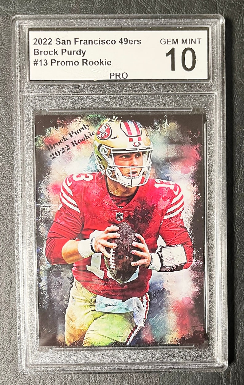 May include: A graded trading card featuring a colorful illustration of Brock Purdy, a football player for the San Francisco 49ers. The card is labeled "2022 San Francisco 49ers Brock Purdy #13 Promo Rookie" and "GEM MINT 10".