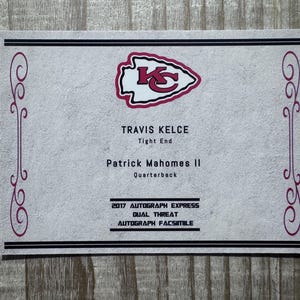 May include: A white card with a red Kansas City Chiefs logo. The card has the text "TRAVIS KELCE Tight End" and "Patrick Mahomes II Quarterback" and "2017 AUTOGRAPH EXPRESS DUAL THREAT AUTOGRAPH FACSIMILE".