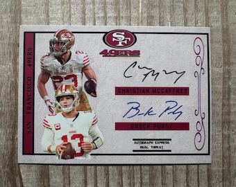 Könnte beinhalten: Eine weiße und rote Football-Karte mit zwei Spielern der San Francisco 49ers, Christian McCaffrey und Brock Purdy. Die Karte zeigt das Teamlogo und den Text "Autograph Express Dual Threat".