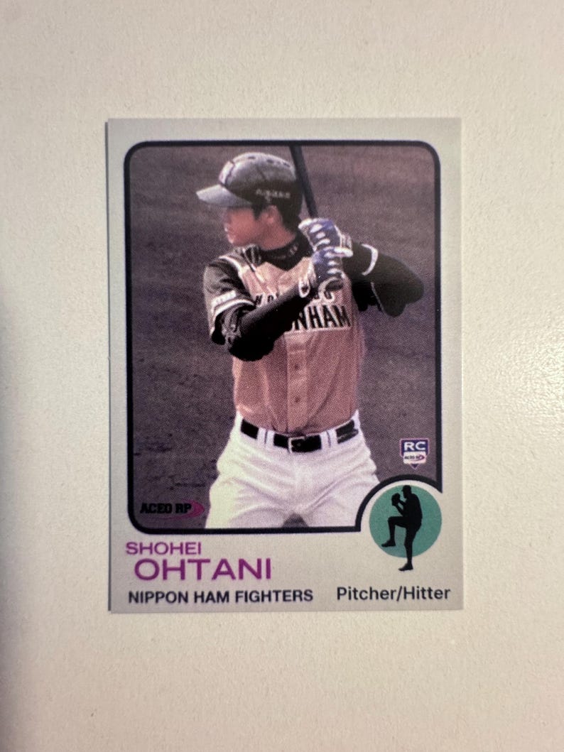 May include: Baseball card featuring Shohei Ohtani of the Nippon Ham Fighters. The card shows Ohtani in a baseball uniform, holding a bat. The card has a retro design with text that includes "Shohei Ohtani" and "Pitcher/Hitter".