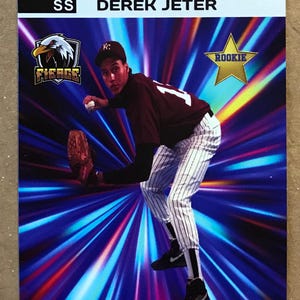 May include: A baseball card featuring Derek Jeter, a rookie player for the Kalamazoo  Fierce in 1991. The card has a blue, purple, and red background with a star-shaped rookie logo. Jeter is wearing a white and black striped uniform with a maroon jersey and a black cap with a white "K" on it. He is throwing a baseball with a serious expression on his face.