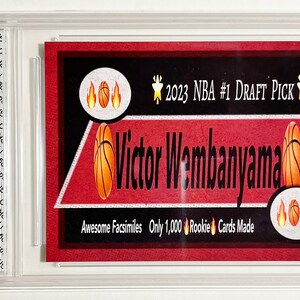 Puede incluir: Una tarjeta de baloncesto roja y blanca con una imagen de Victor Wembanyama, el #1 del Draft de la NBA 2023. La tarjeta dice "Awesome Facsimiles Only 1,000 Rookie Cards Made".