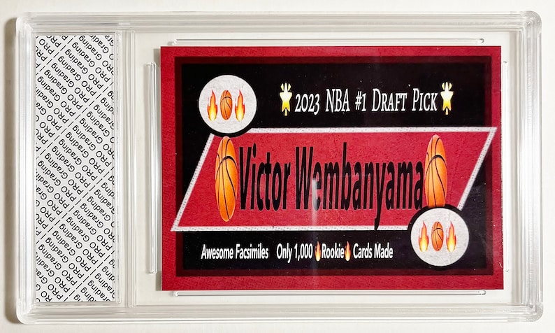 Puede incluir: Una tarjeta de baloncesto roja y blanca con una imagen de Victor Wembanyama, el #1 del Draft de la NBA 2023. La tarjeta dice "Awesome Facsimiles Only 1,000 Rookie Cards Made".