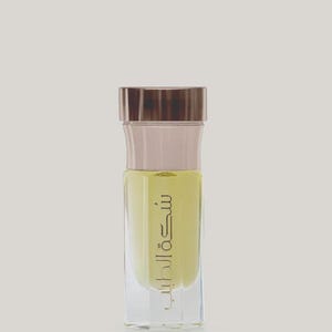 Pode incluir: Um frasco de perfume de vidro transparente com uma tampa castanha e um líquido amarelo claro no interior. O frasco tem escrita árabe dourada na frente. O frasco tem uma forma retangular com bordas arredondadas.