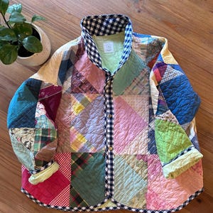 May include: A patchwork jacket with a variety of colorful fabric squares. The jacket features a black and white checkered collar and trim, with a button-up front. The sleeves and body are made of different patterned fabrics.