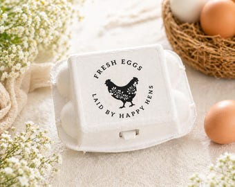 May include: A white egg carton with the text "FRESH EGGS LAID BY HAPPY HENS" and a black hen illustration. The carton contains white eggs. A woven basket with brown and white eggs is in the background.