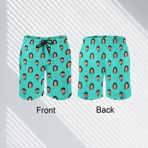 May include: A pair of turquoise swim trunks with a repeated pattern of a man's face. The front and back of the trunks are shown.