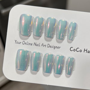 May include: Set of ten iridescent white press-on nails with a subtle shimmer. The nails are arranged in two rows on a white card with the text "Your Online Nail Art Designer" and "CoCo Ha" printed on it.