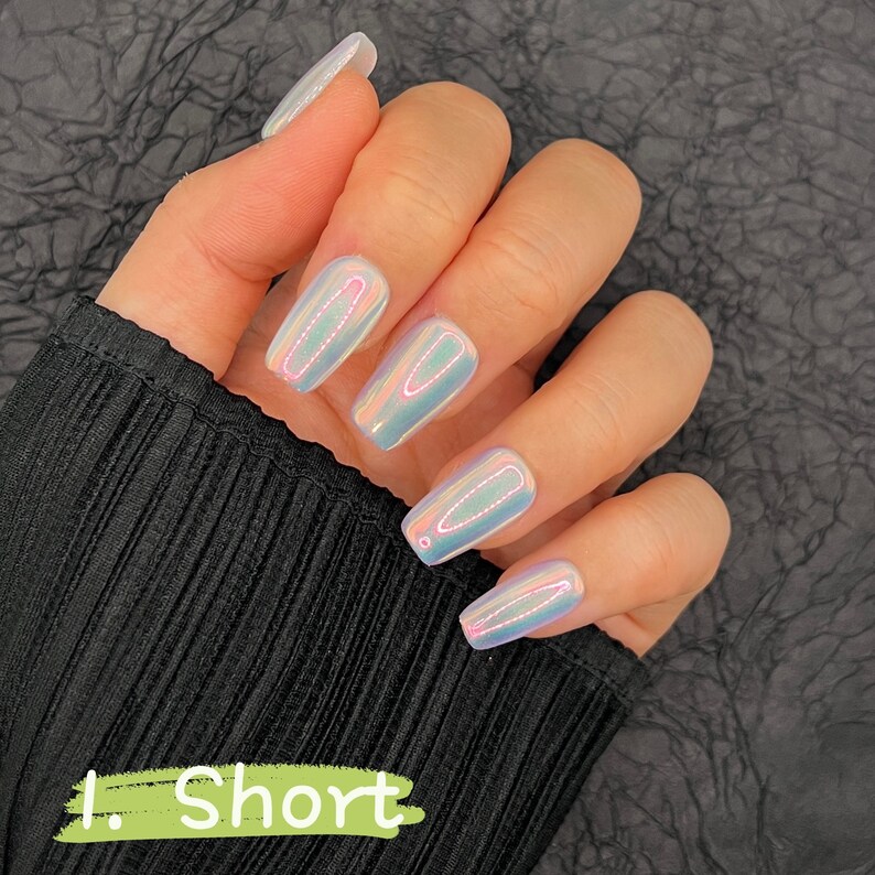 May include: Close-up of a hand with short, iridescent, coffin-shaped nails. The nails are painted with a holographic polish that shifts color in the light.