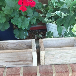 May include: Two rustic wooden planter boxes with white painted edges. The boxes are empty and sitting on a brick surface.