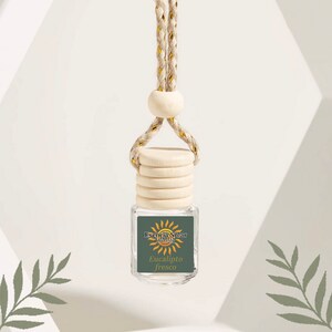 May include: A small, clear glass bottle with a wooden cap and a hanging cord. The bottle has a label with the text "Esencia Solar Barcelona" and "Eucalipto fresco". The cord is beige with gold accents.